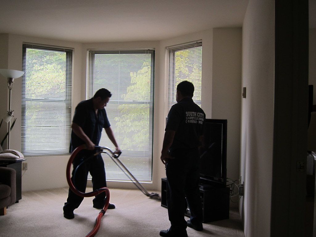 Two technicians cleaning a living room carpet with a hose and wand