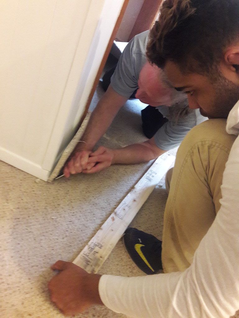Two installers working carpet into the tack strip along a wall